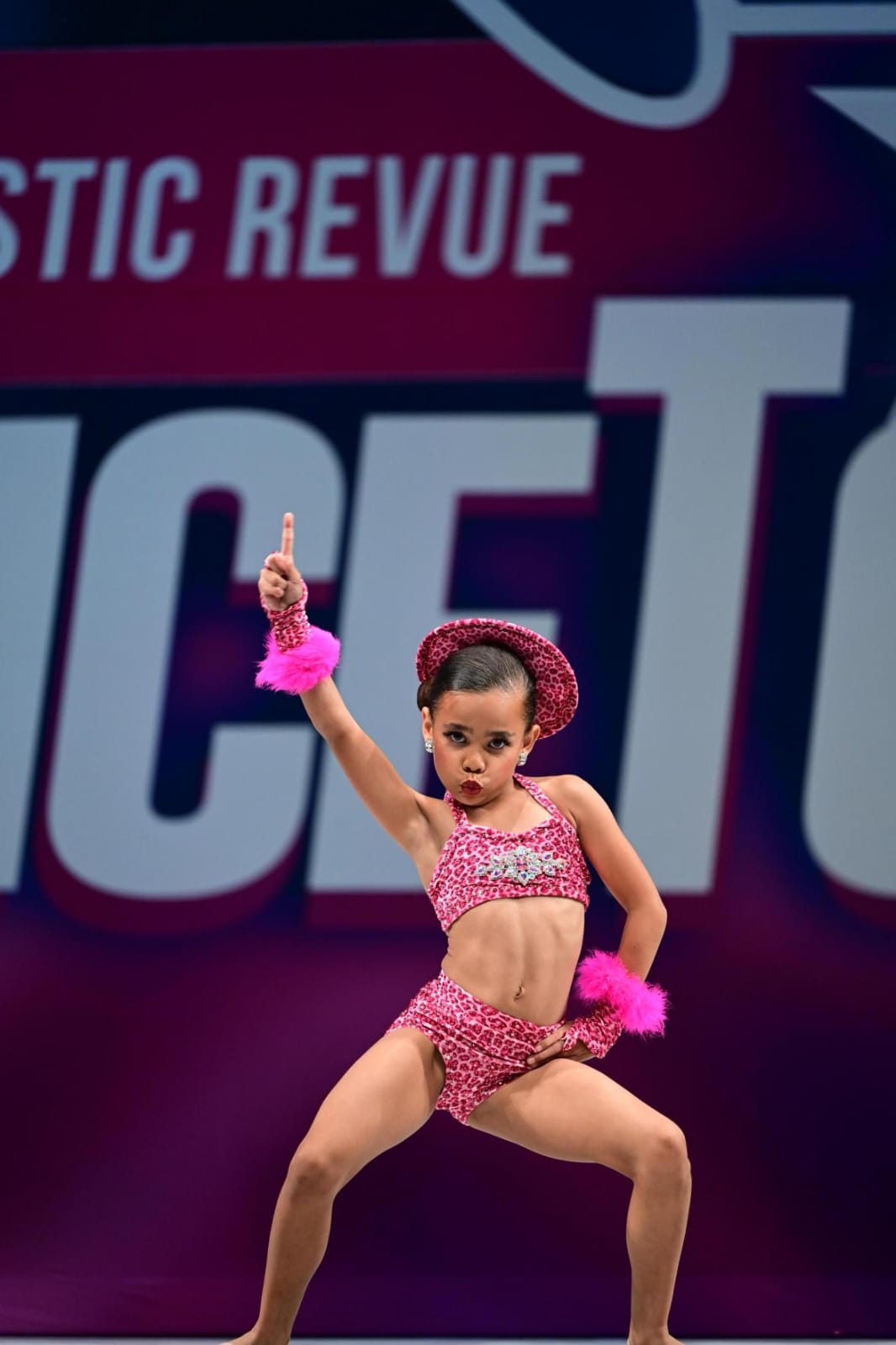 Jayla mid-solo, pointing to the sky in her pink leopard costume